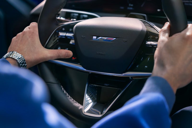 Close-up of a Man About to Press the V-Button on the 2026 OPTIQ-V Steering Wheel | C. Harper Cadillac in Belle Vernon PA